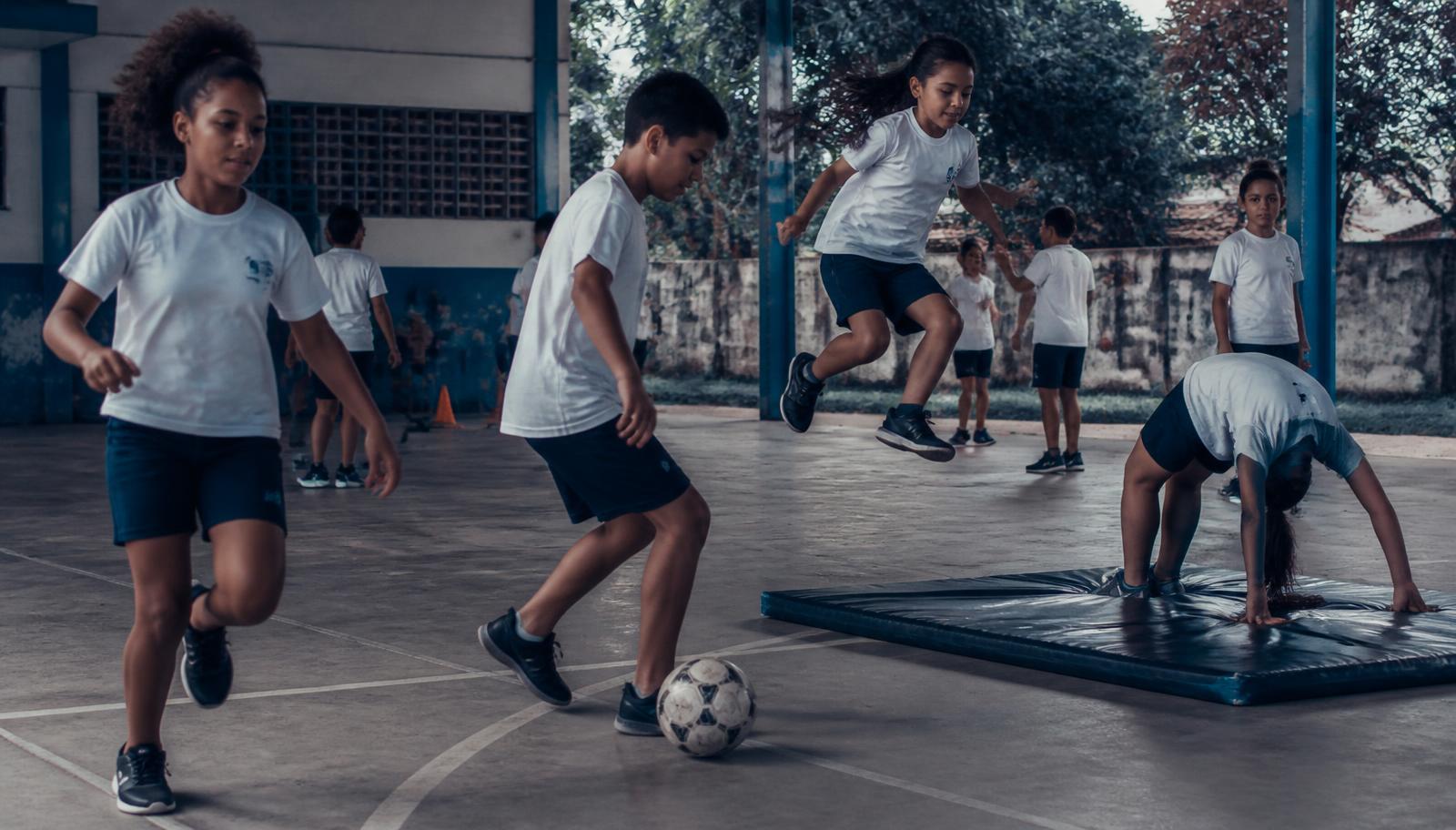 Crianças e adolescentes praticando diferentes modalidades esportivas em uma quadra escolar